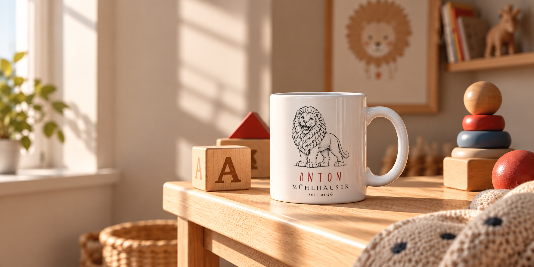 Weiße ORTSWERK-Kindertasse mit Löwen-Zeichnung und den Zeilen ANTON, MÜHLHÄUSER seit 2026 auf einem Holztisch in einem hellen Kinderzimmer, mit Fenster und Zimmerpflanze links, Bauklötzen, Stapelspielzeug und gestrickter Decke